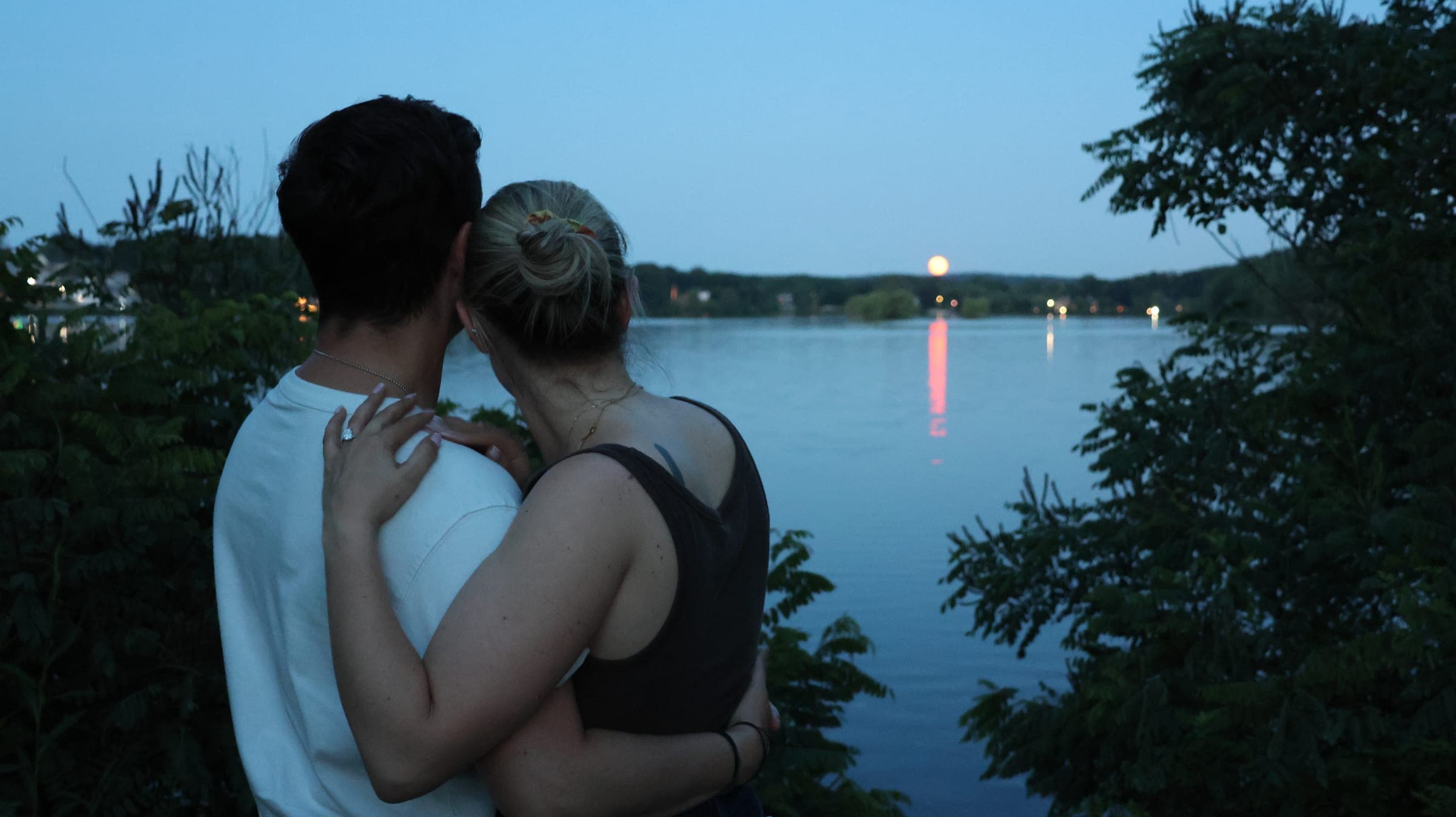Jake and Sarah embracing at Horn Pond under the pink Strawberry Moon.